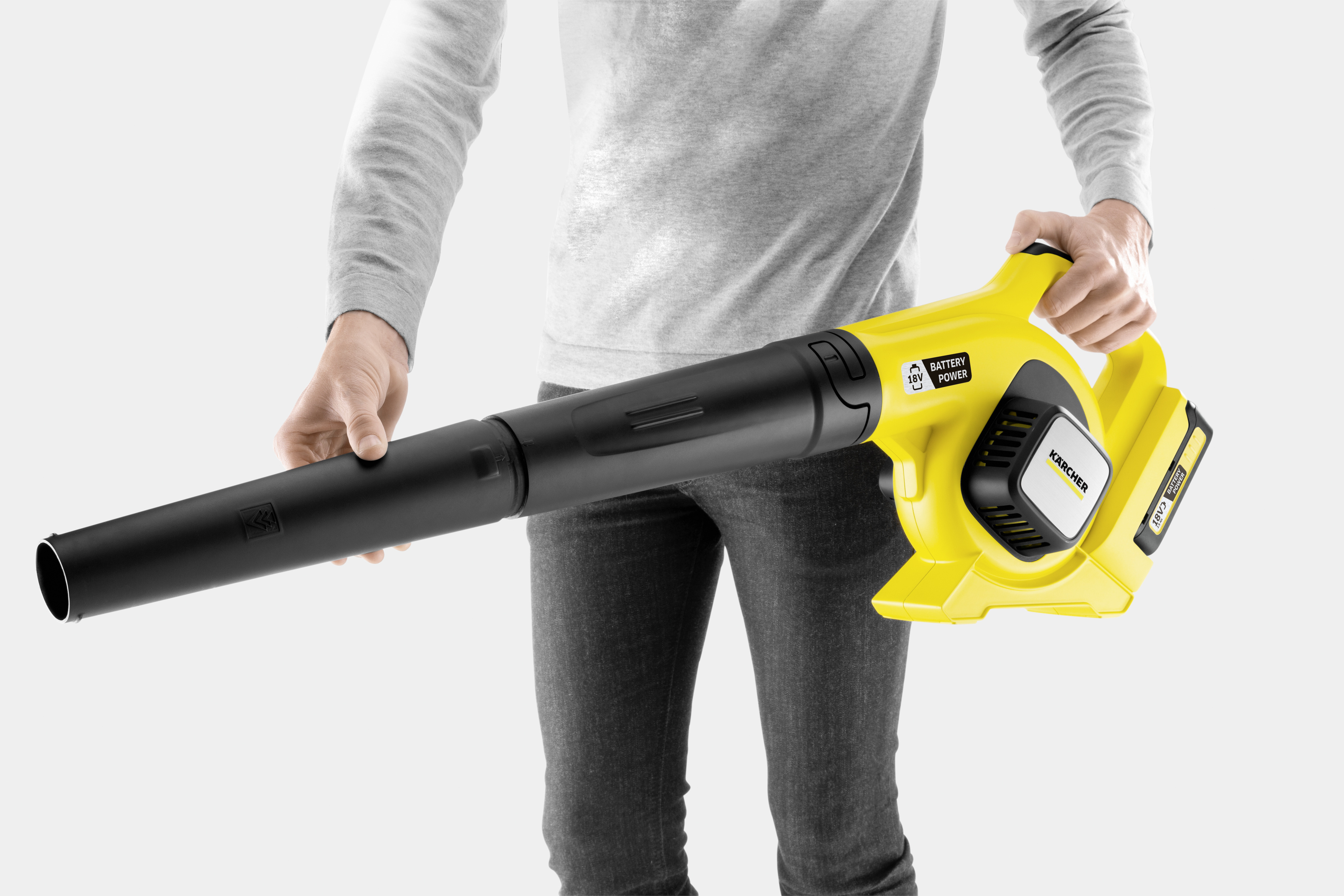 Persona con jersey gris sostiene un soplador de hojas inalámbrico amarillo y negro.