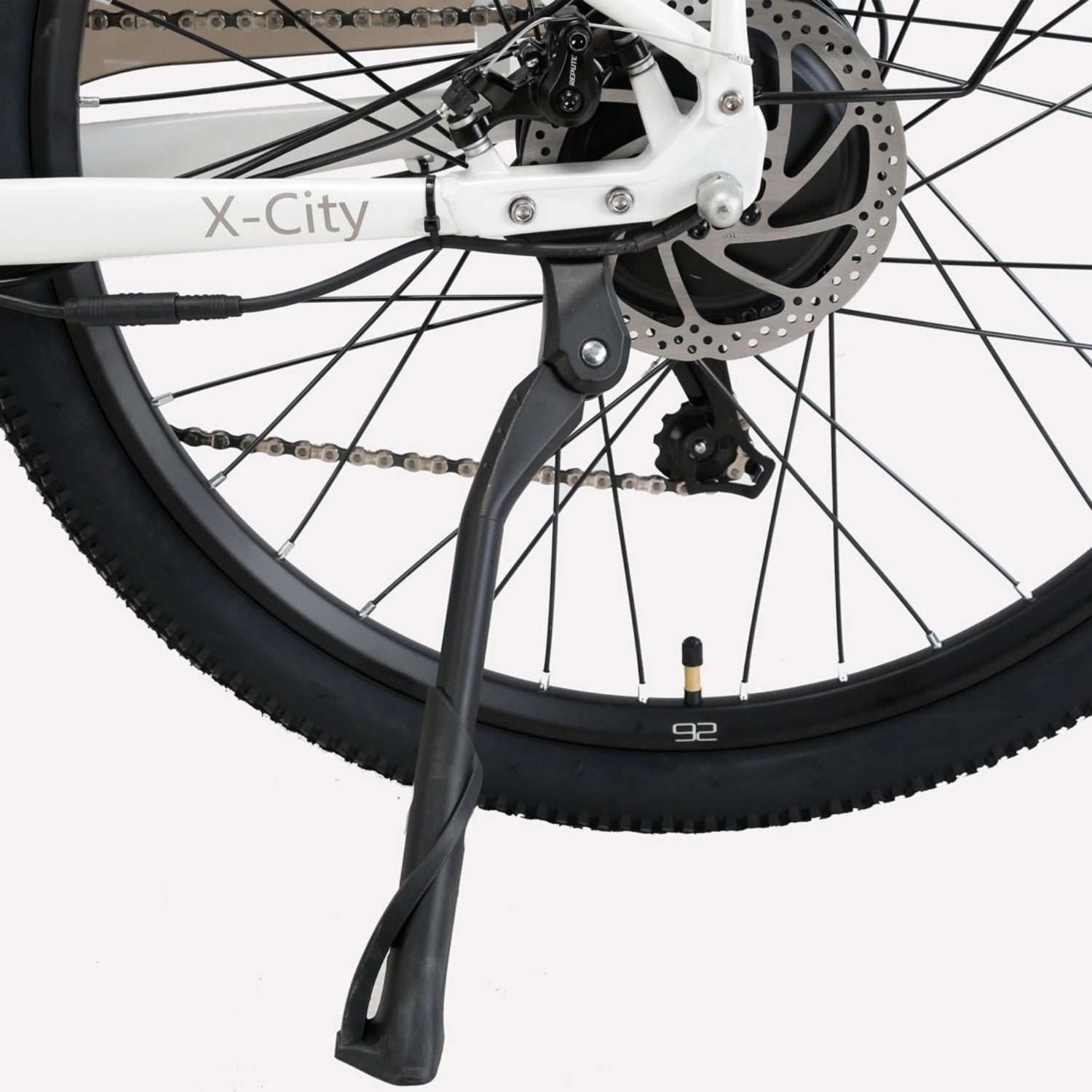 Primo piano della ruota posteriore, telaio, freno a disco, catena e cavalletto nero di una bicicletta bianca.