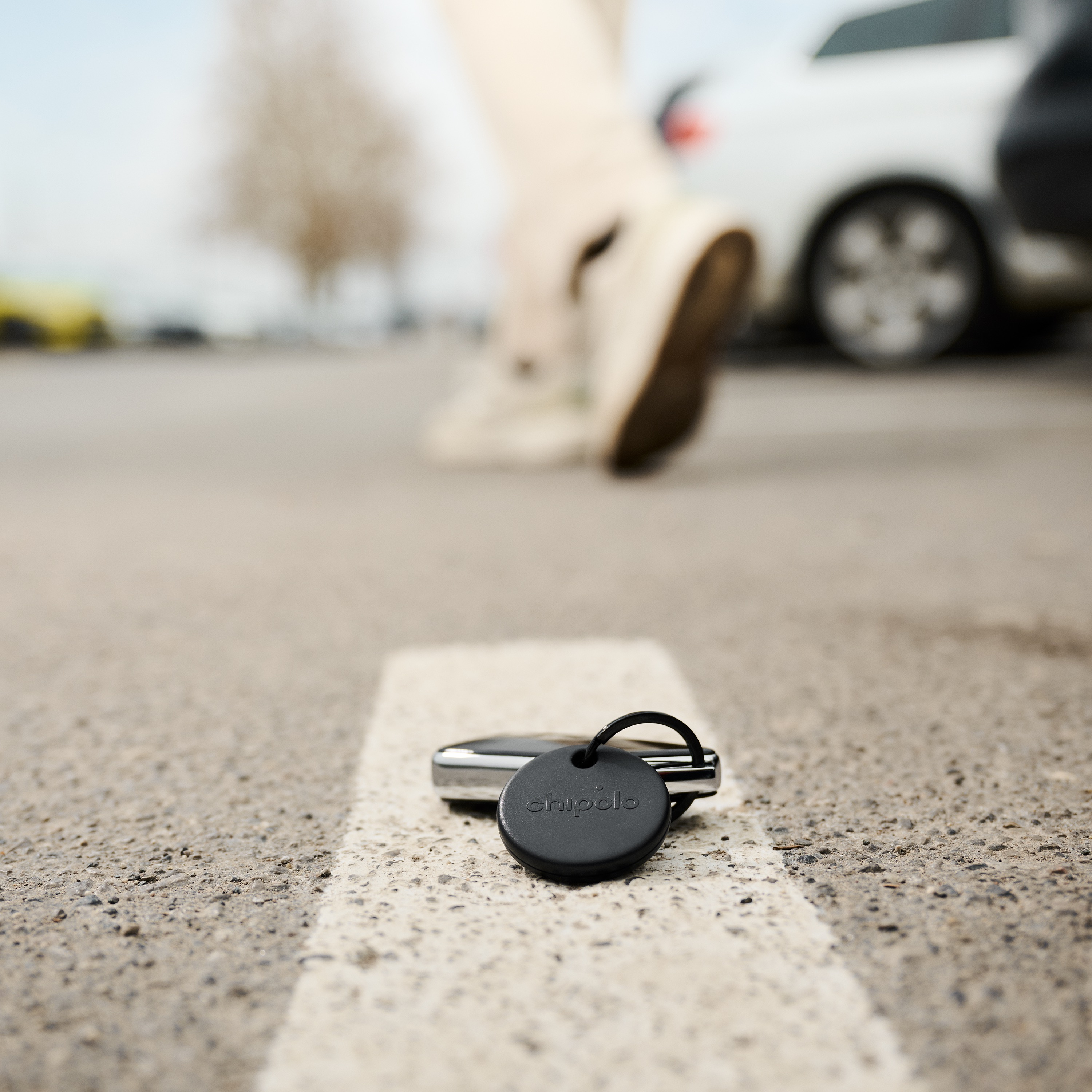Un porte-clés Chipolo noir est posé sur une ligne de stationnement alors qu'une personne s'éloigne.