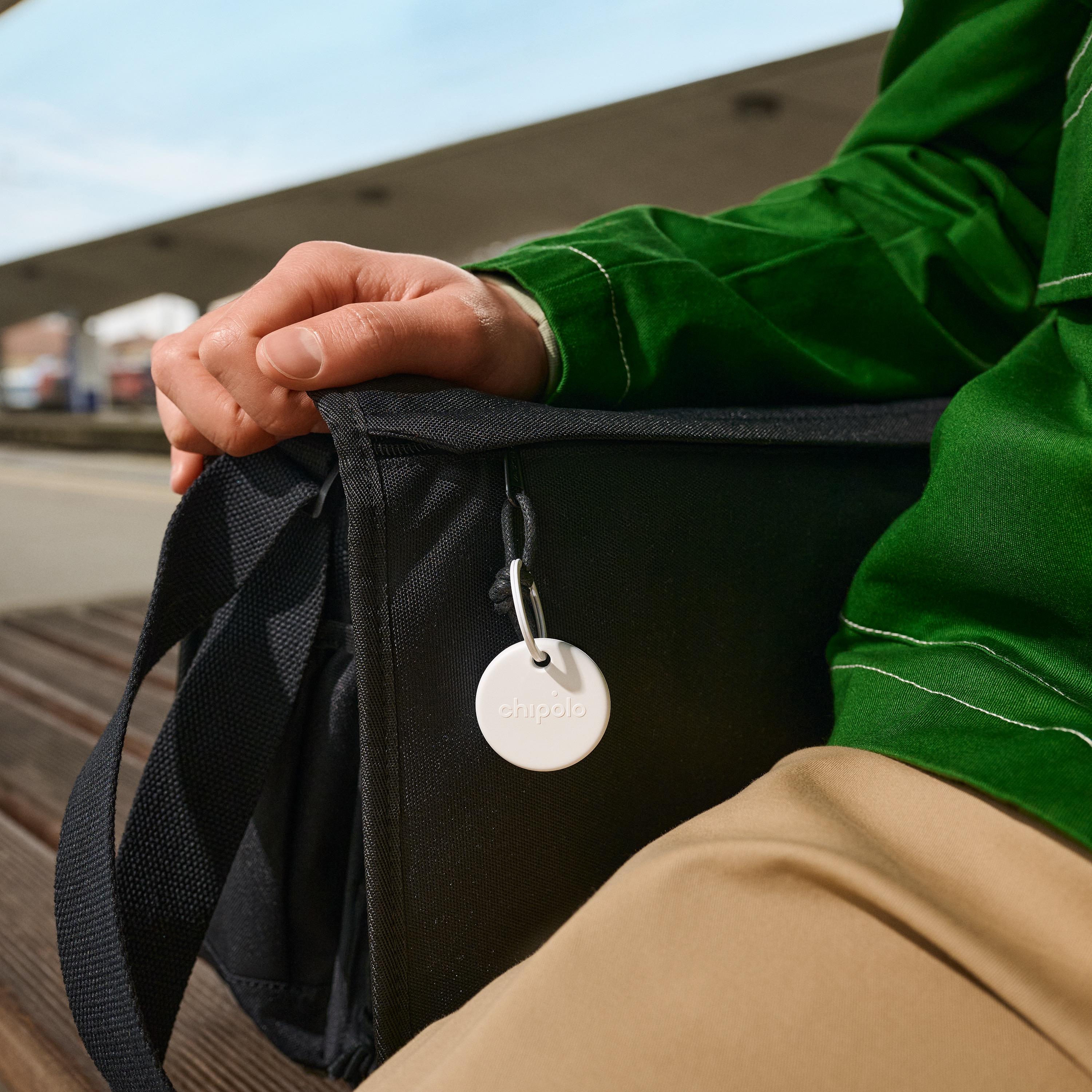 Une main tient un sac noir avec un tracker Chipolo blanc rond attaché.