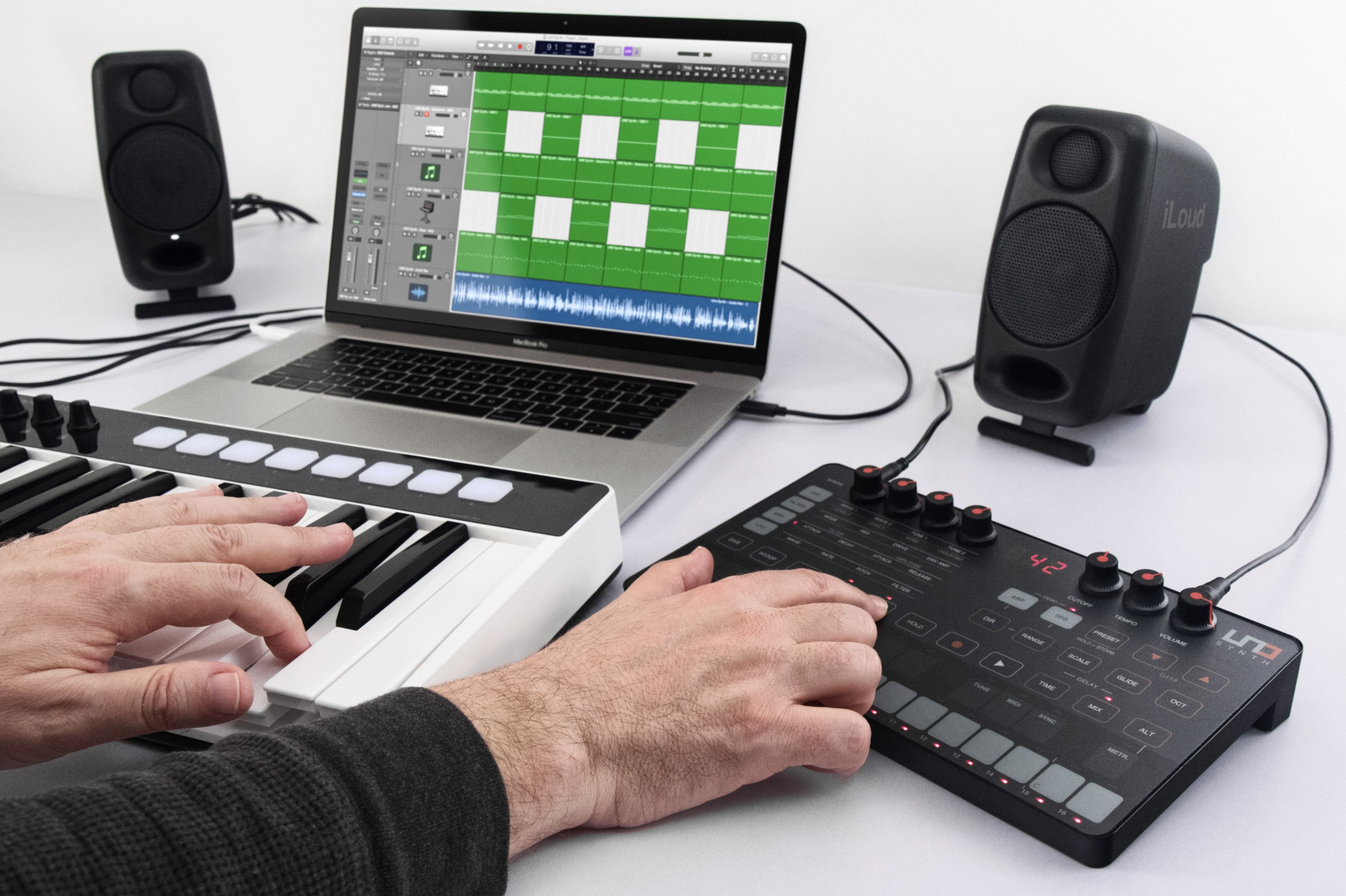 Ein Musiker spielt auf einer MIDI-Tastatur und einem Synthesizer, im Hintergrund ein Laptop mit Musiksoftware und zwei Lautsprecher.