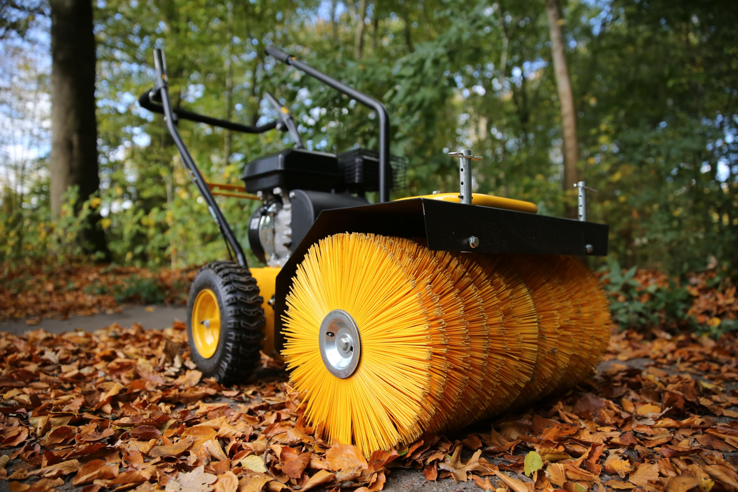 Eine gelbe Kehrmaschine steht auf einem mit Herbstlaub bedeckten Weg im Wald.