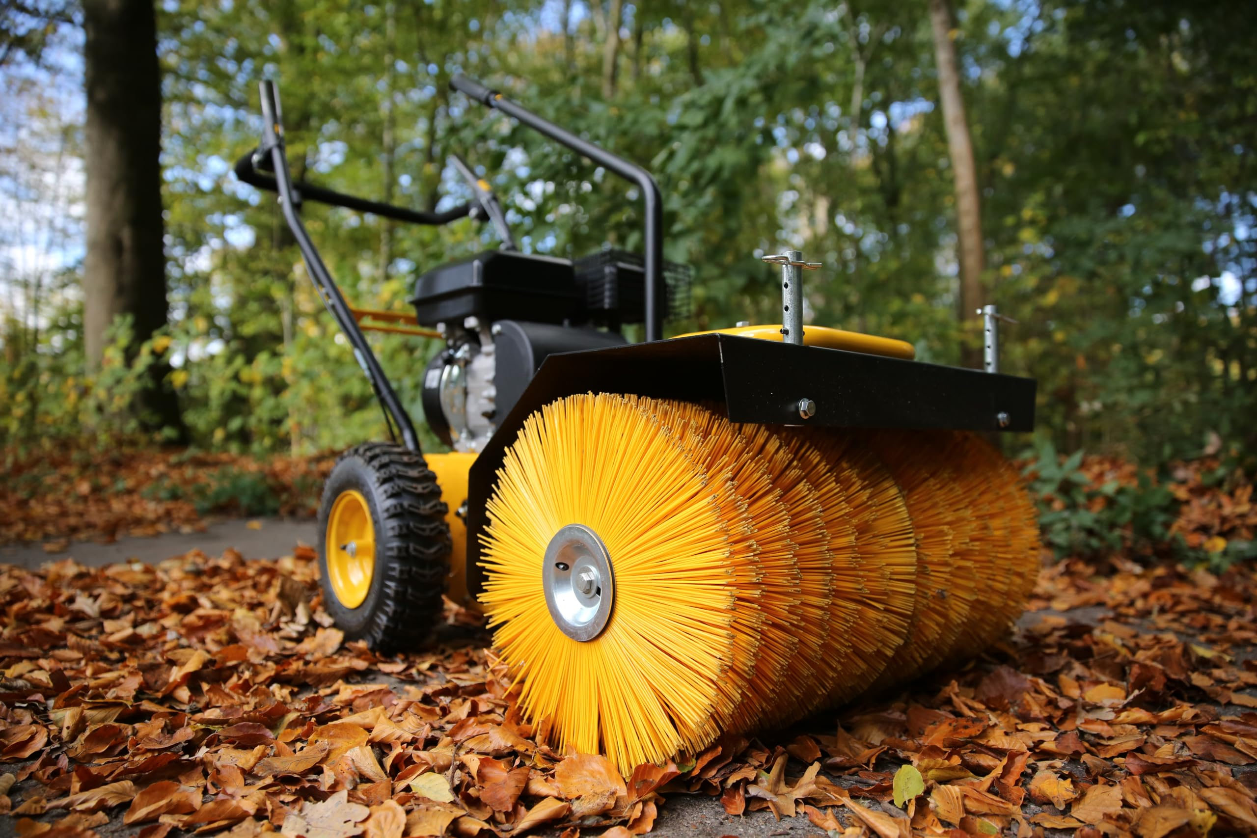 Eine gelb-schwarze motorisierte Kehrmaschine steht draußen auf einem mit Herbstlaub bedeckten Boden.