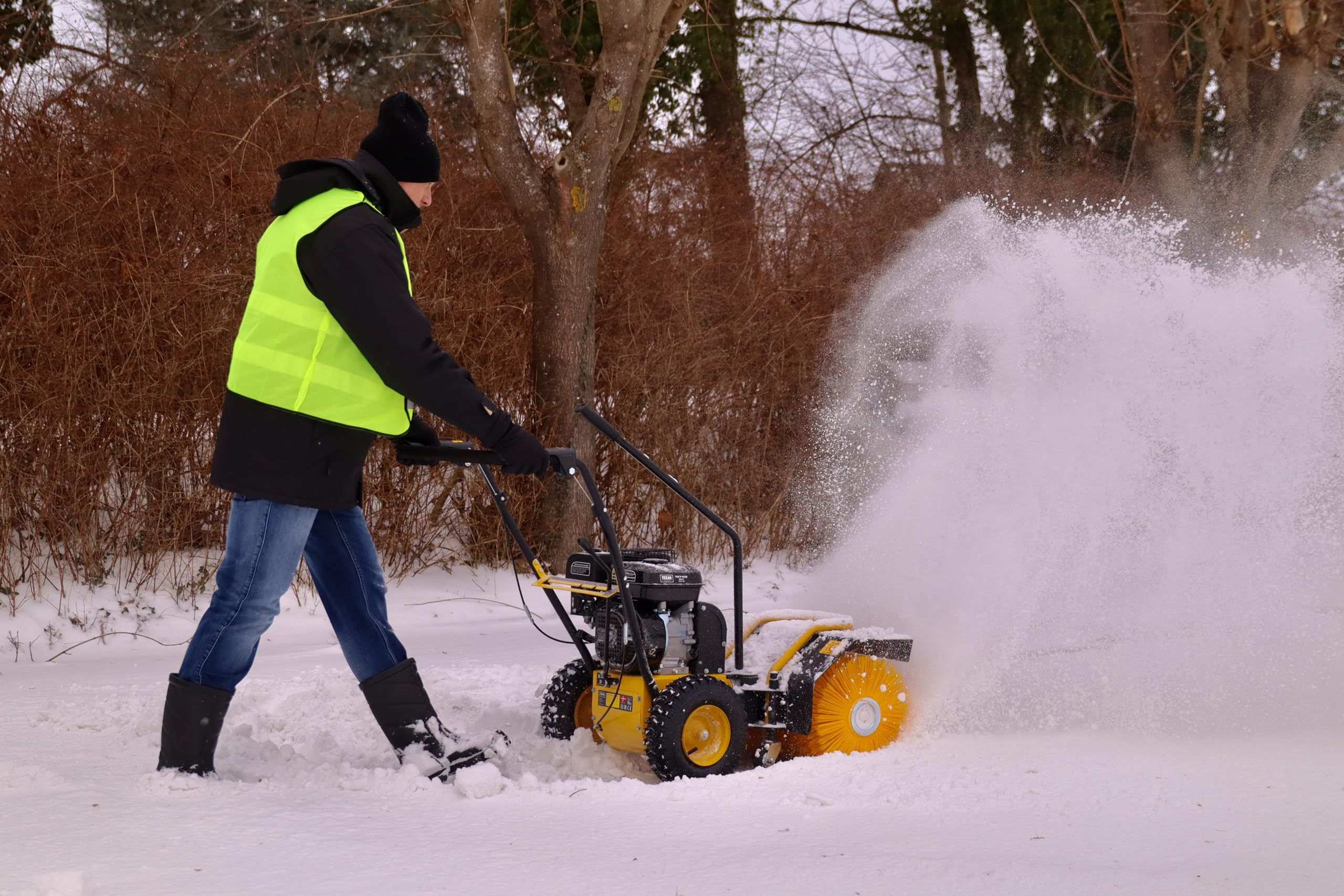 Mann in Warnweste und Mütze bedient eine gelbe Schneefräse im Schnee.