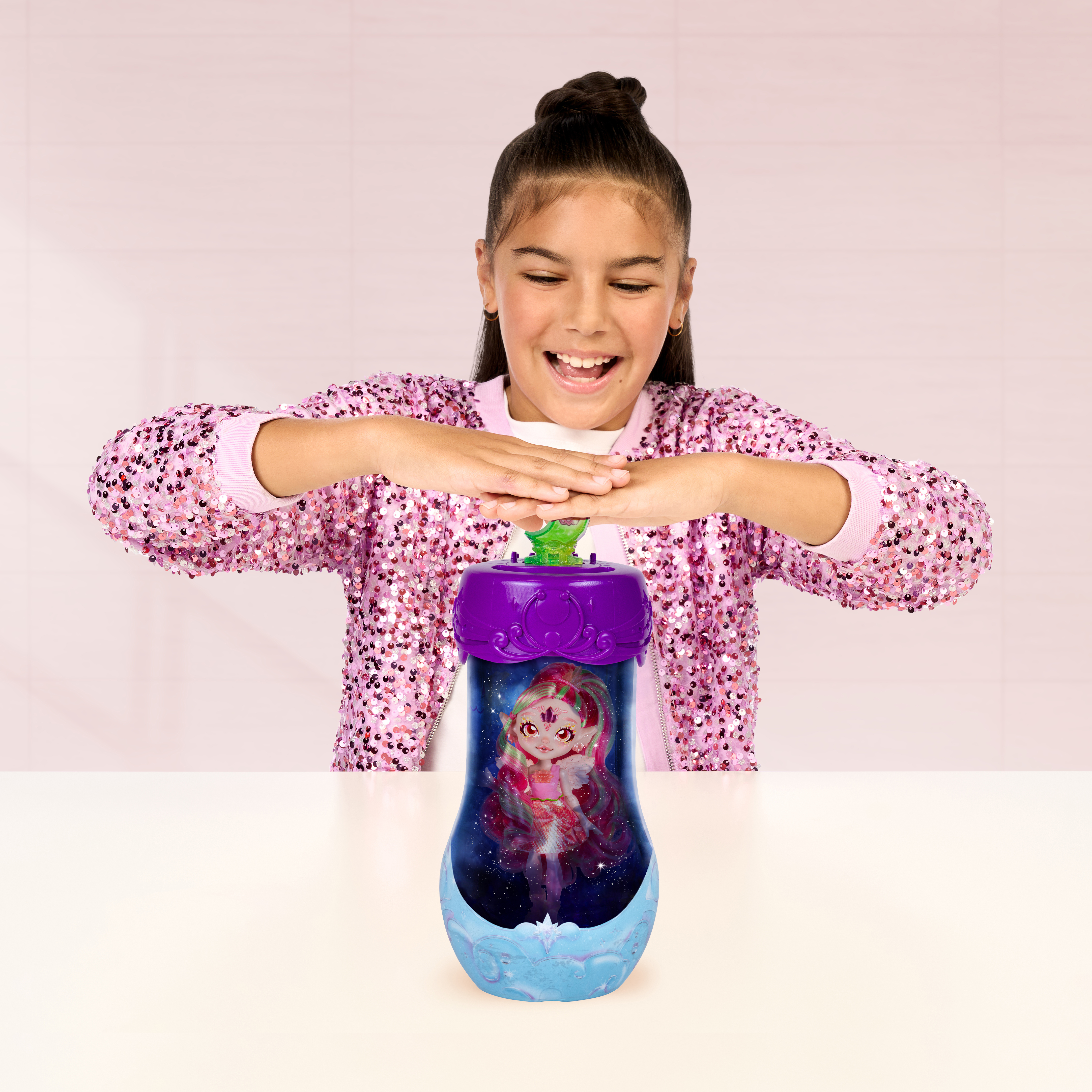 Ein junges Mädchen in einer rosa Paillettenjacke interagiert gl ücklich mit einem magischen Spielzeugbehälter mit Puppe.