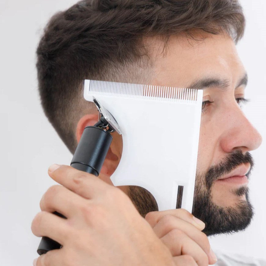 Un uomo usa un tagliacapelli con una guida bianca per modellare la barba.