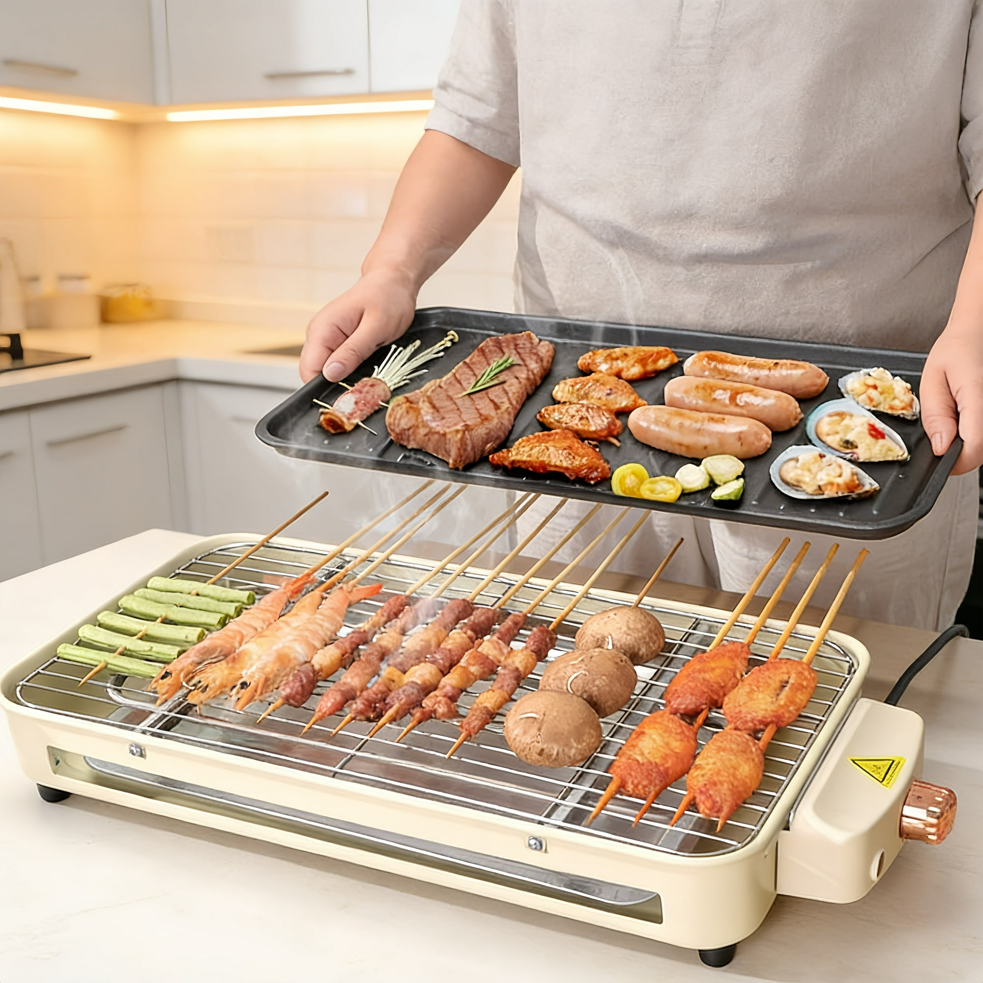 Eine Person hält ein Tablett mit Fleisch und Meeresfrüchten über einem Tischgrill in einer Küche.