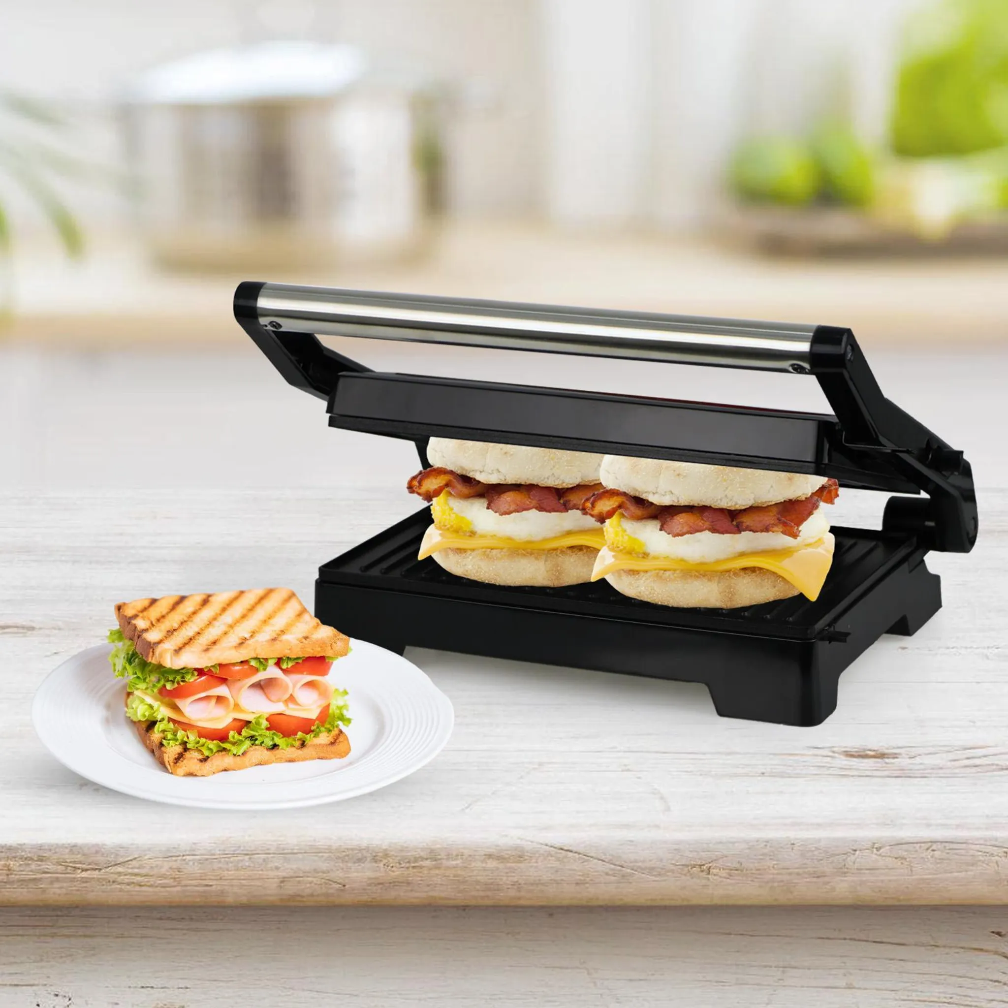 Ein Sandwichmaker presst Frühstückssandwiches, während ein fertiges Sandwich auf einem Teller daneben liegt.