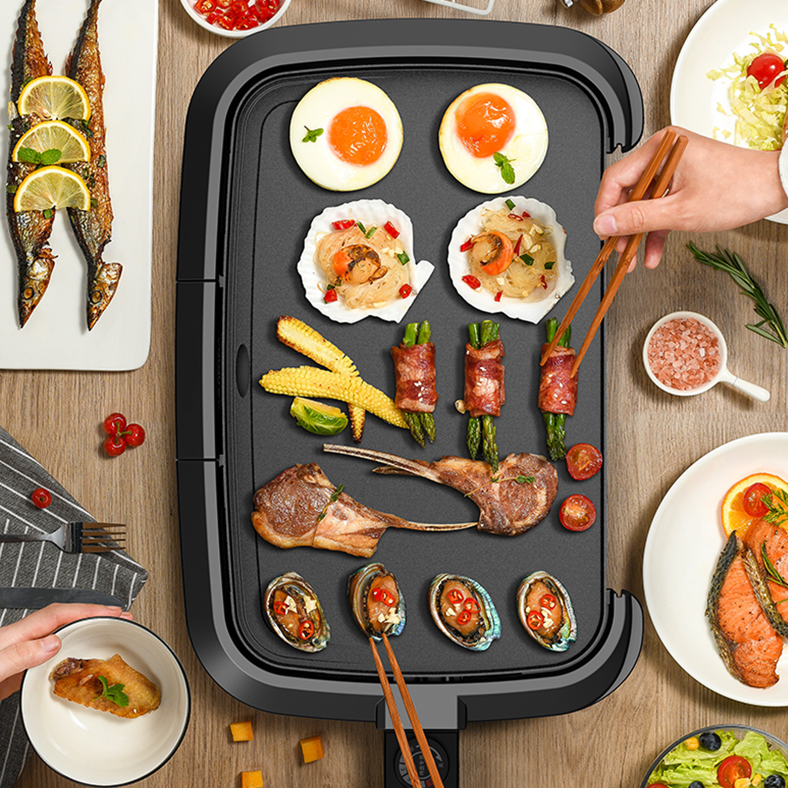 Ein elektrischer Grill auf einem Tisch mit gebratenem Fleisch, Eiern, Muscheln, Gemüse und Fischgerichten.