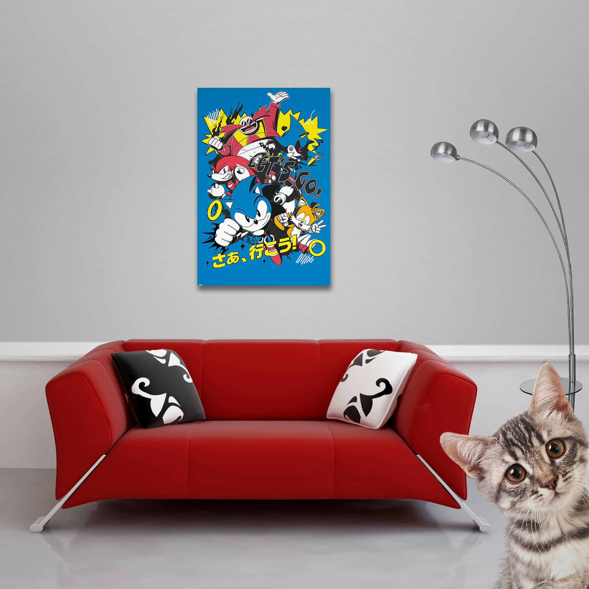 Ein rotes Sofa mit Kissen steht vor einer grauen Wand mit Sonic-Poster, rechts schaut eine Katze hervor.