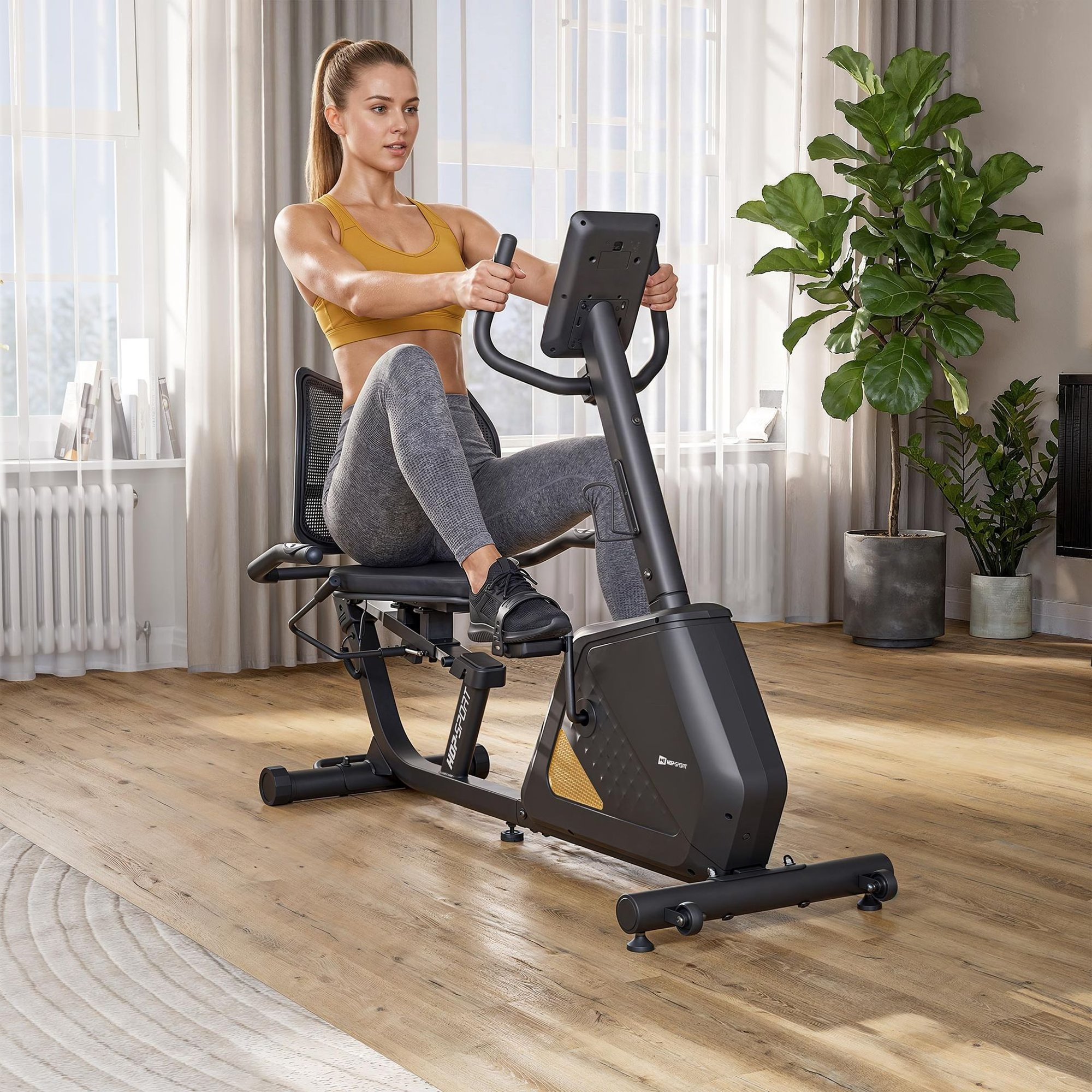 Eine Frau in Sportkleidung trainiert auf einem Liegeheimtrainer in einem hellen Zimmer mit Pflanzen.