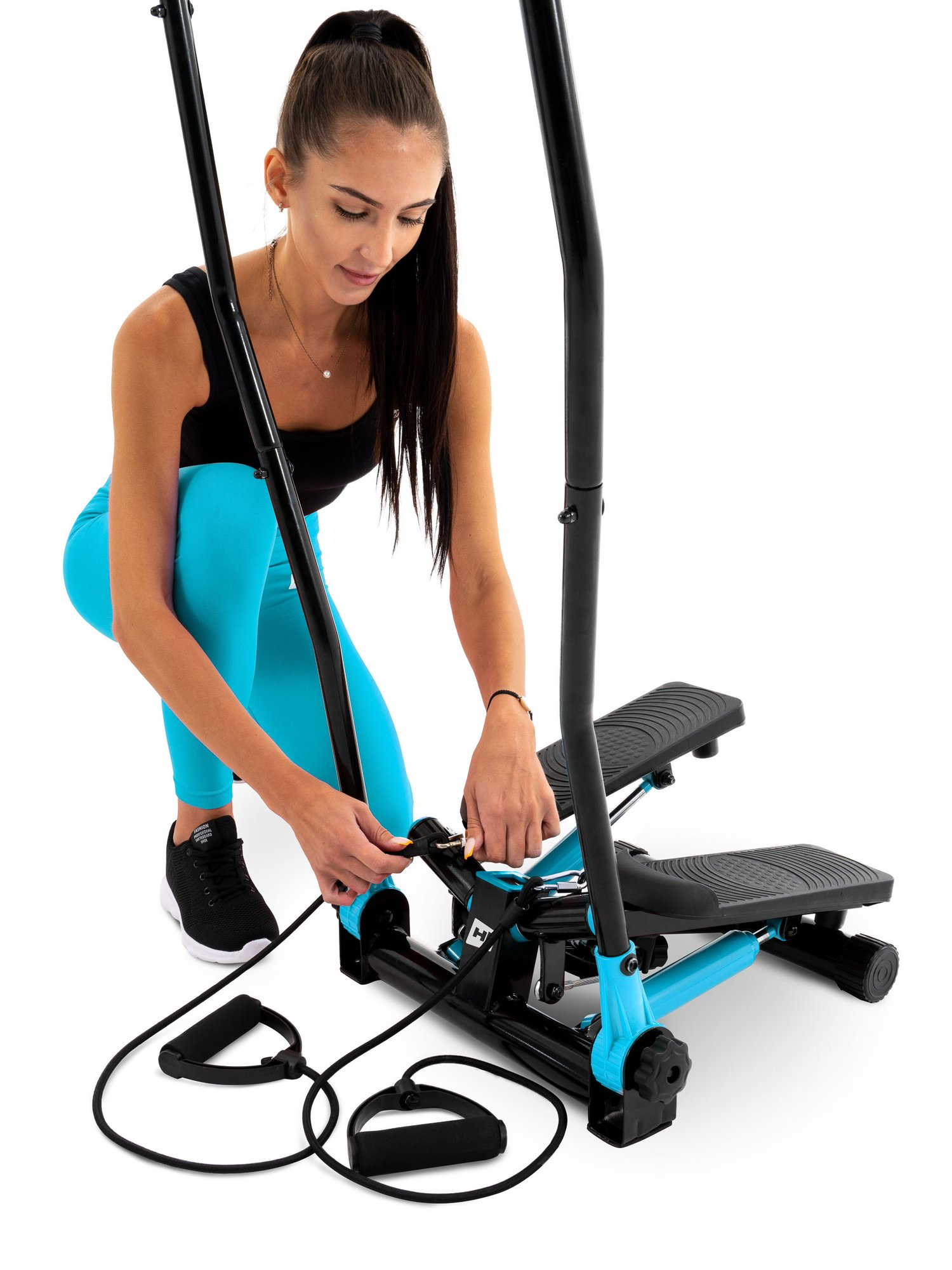 Eine Frau in blauen Leggings und schwarzem Top bereitet einen schwarz-blauen Stepper mit Widerstandsbändern vor.