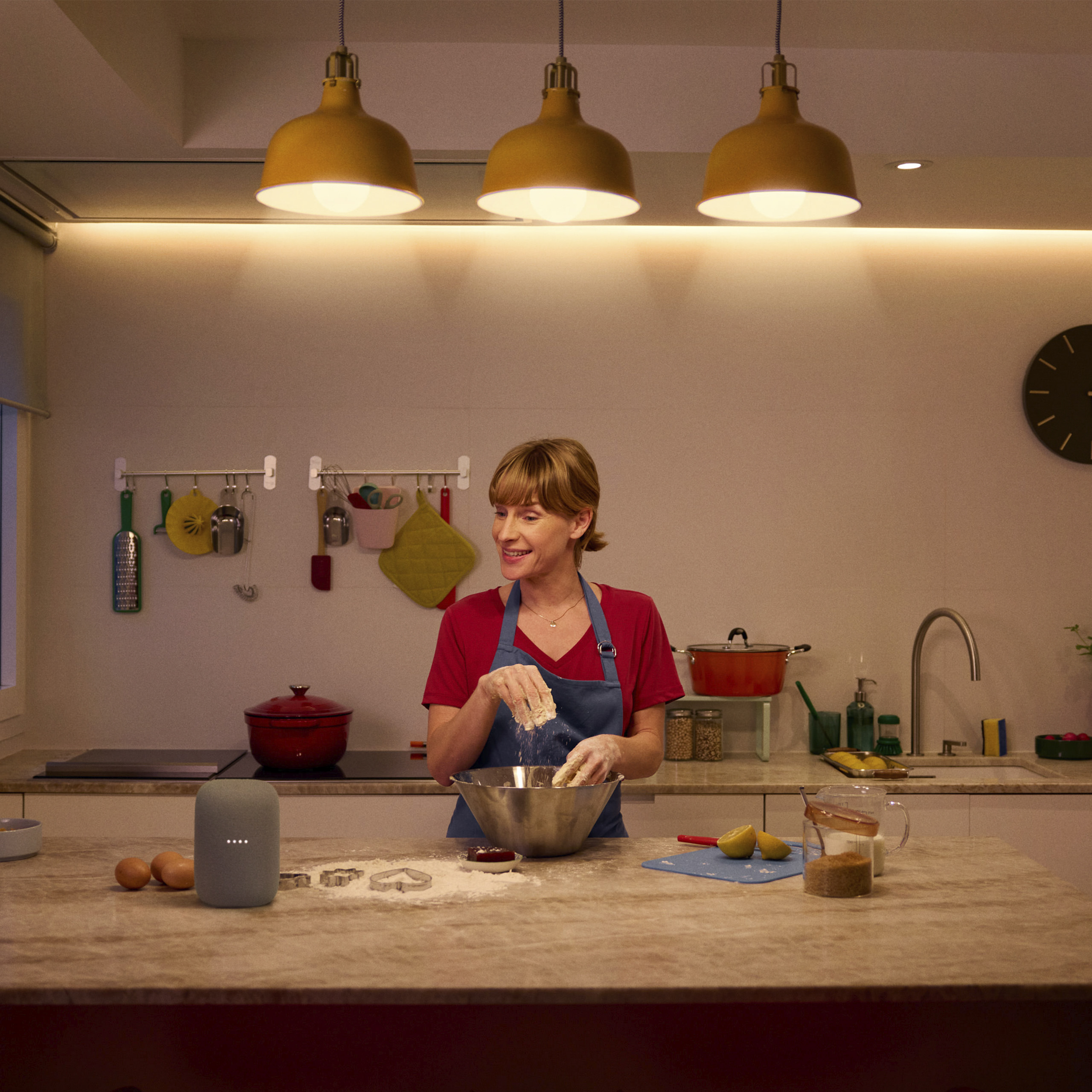 Een vrouw in een blauw schort staat in een lichte keuken en kneedt deeg in een kom.