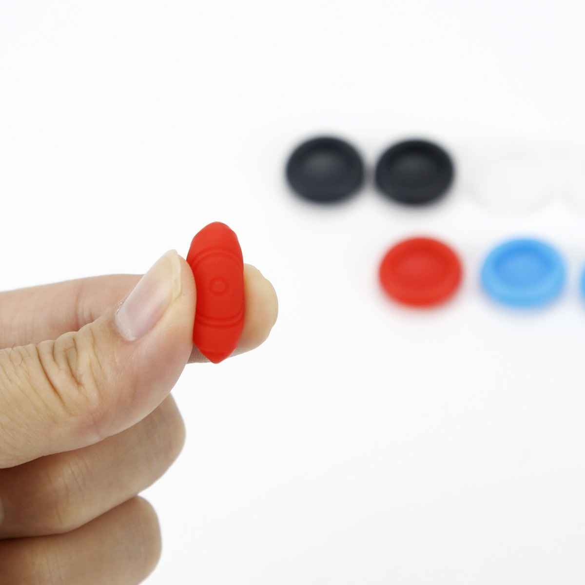 Una mano tiene un cappuccio per joystick in silicone rosso, con cappucci colorati sfocati sullo sfondo.