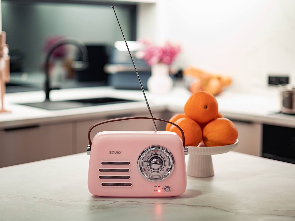 Różowe radio w stylu retro z anteną stoi na blacie kuchennym obok talerza pomarańczy.