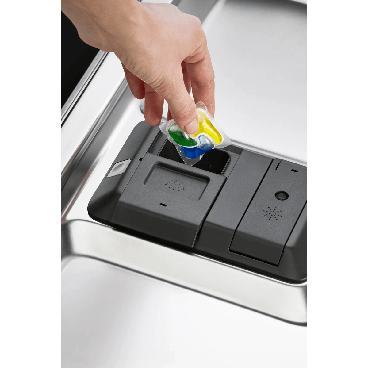 Una mano coloca una pastilla de lavavajillas de colores en el dispensador.
