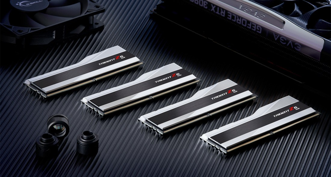 Vier silber-schwarze Trident Z5 RAM-Riegel auf dunkler Rillenoberfläche mit Computerteilen im Hintergrund.