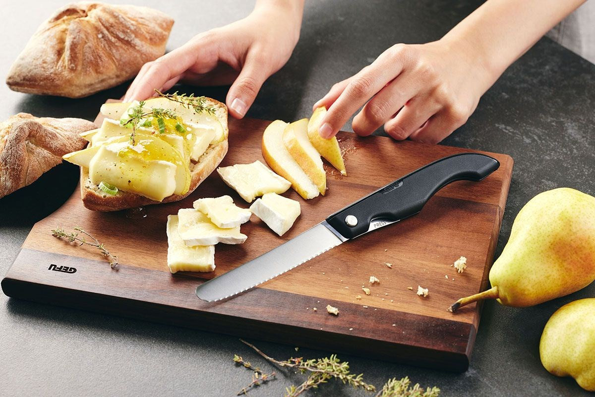 Hände bereiten ein Sandwich mit Käse und Birnenscheiben auf einem Holzbrett vor, daneben ein Messer.