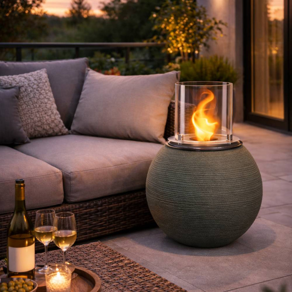 Accogliente patio con un caminetto da tavolo verde rotondo, un divano con cuscini e una bottiglia di vino con due bicchieri.