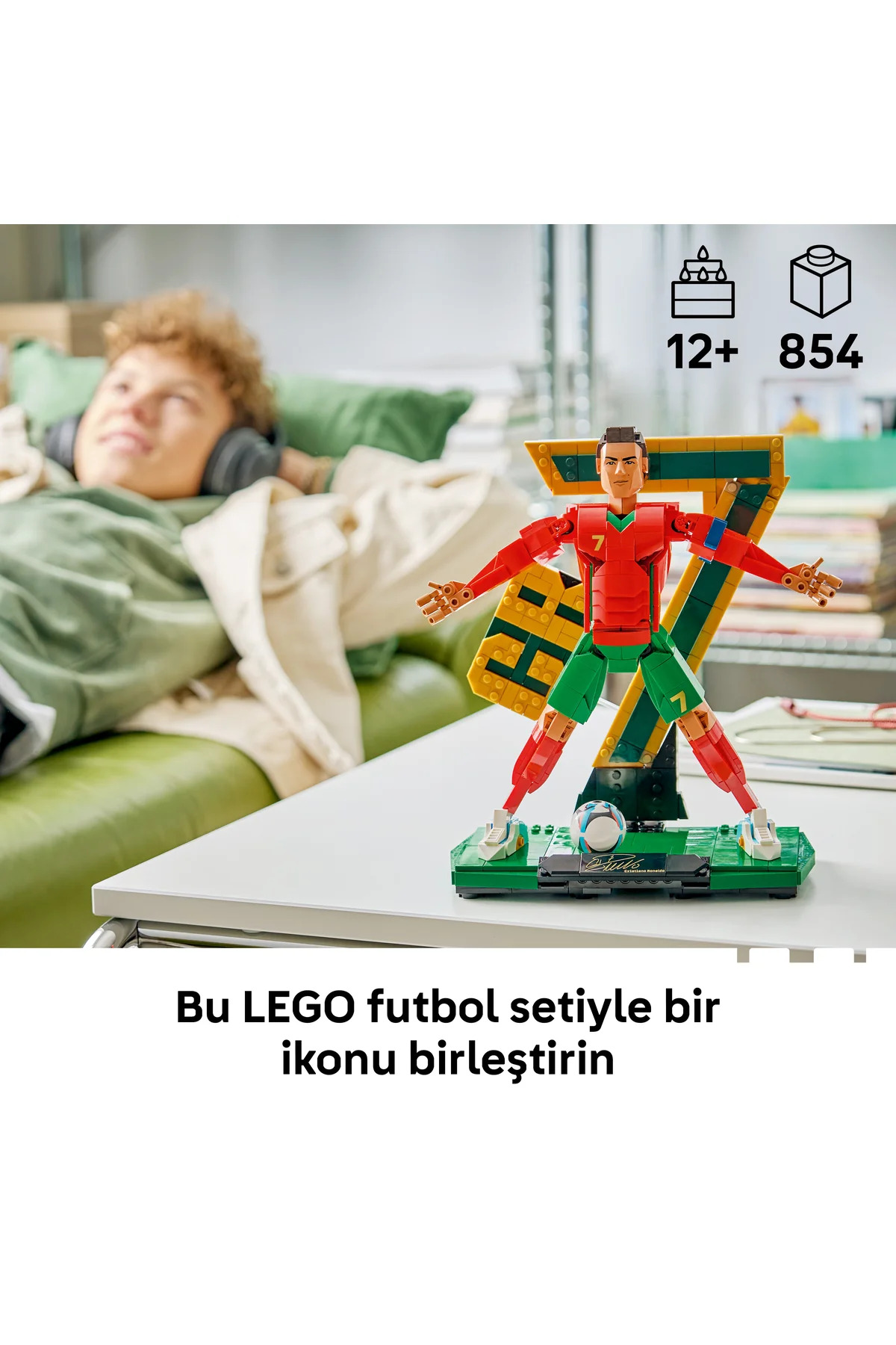 Bir masada duran Lego Cristiano Ronaldo figürü ve arka planda yeşil kanepede dinlenen bir kişi.