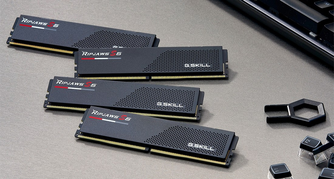 Quatre barrettes de RAM G.Skill Ripjaws S5 noires reposent sur une surface grise à côté d'un clavier.