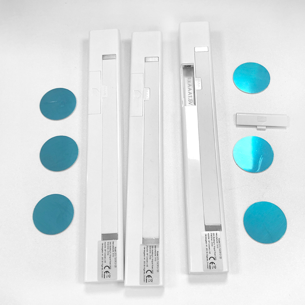 Tre luci LED bianche per armadio con cuscinetti adesivi blu e un vano batteria.