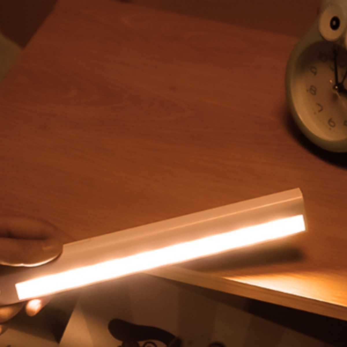 Una mano tiene una barra luminosa a LED bianca e luminosa sopra una scrivania di legno.