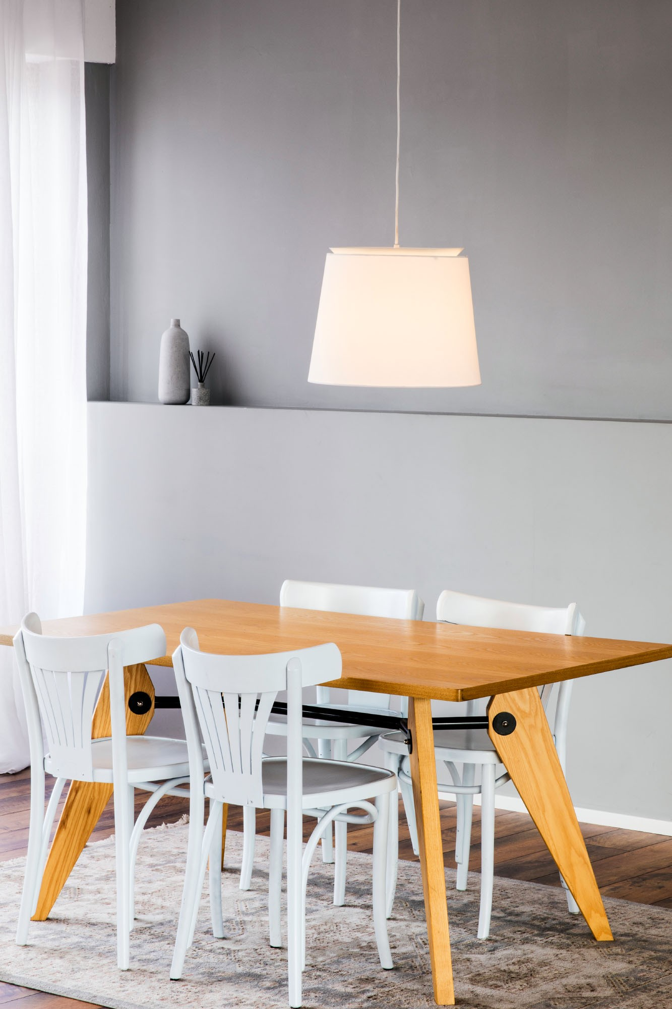 Un tavolo da pranzo in legno con sedie bianche si trova su un tappeto sotto una lampada a sospensione.