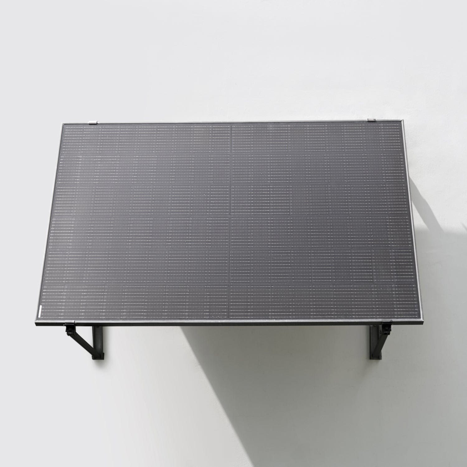 Un pannello solare scuro montato su una parete bianca liscia, sostenuto da due staffe nere.