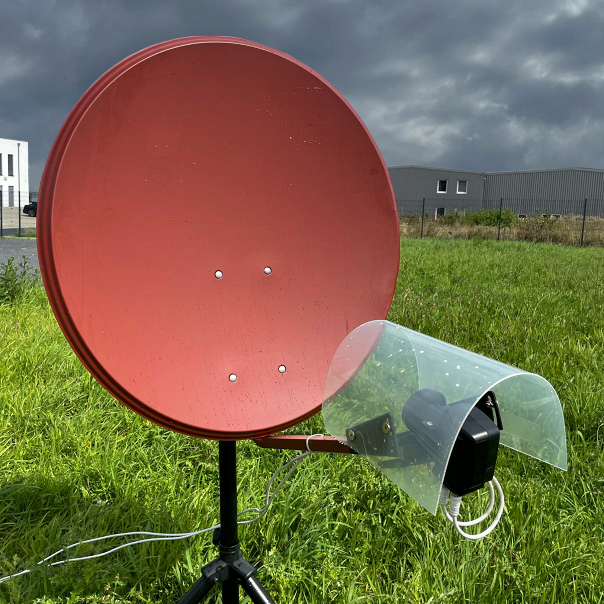 Eine rote Satellitenschüssel steht auf einer grünen Wiese unter einem dunklen, bewölkten Himmel.