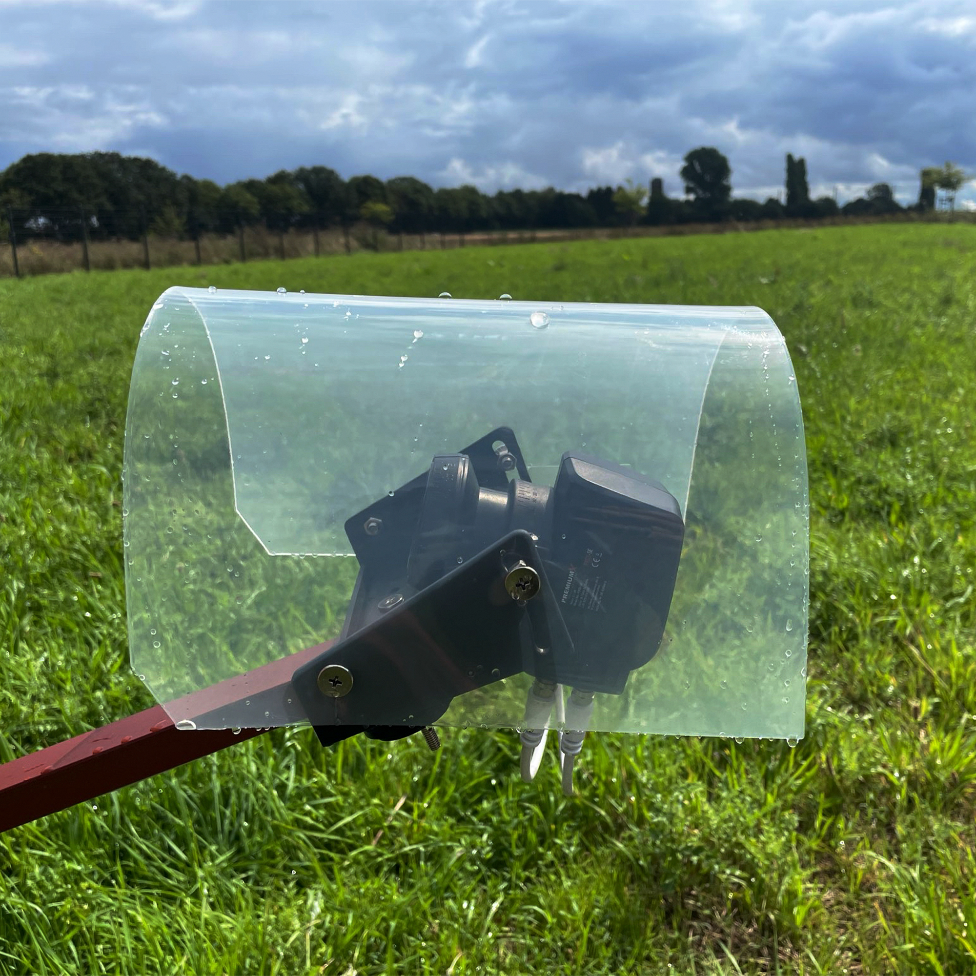 Eine Satellitenantennen-LNB unter einer gebogenen transparenten Regenschutzabdeckung über einer grünen Wiese.