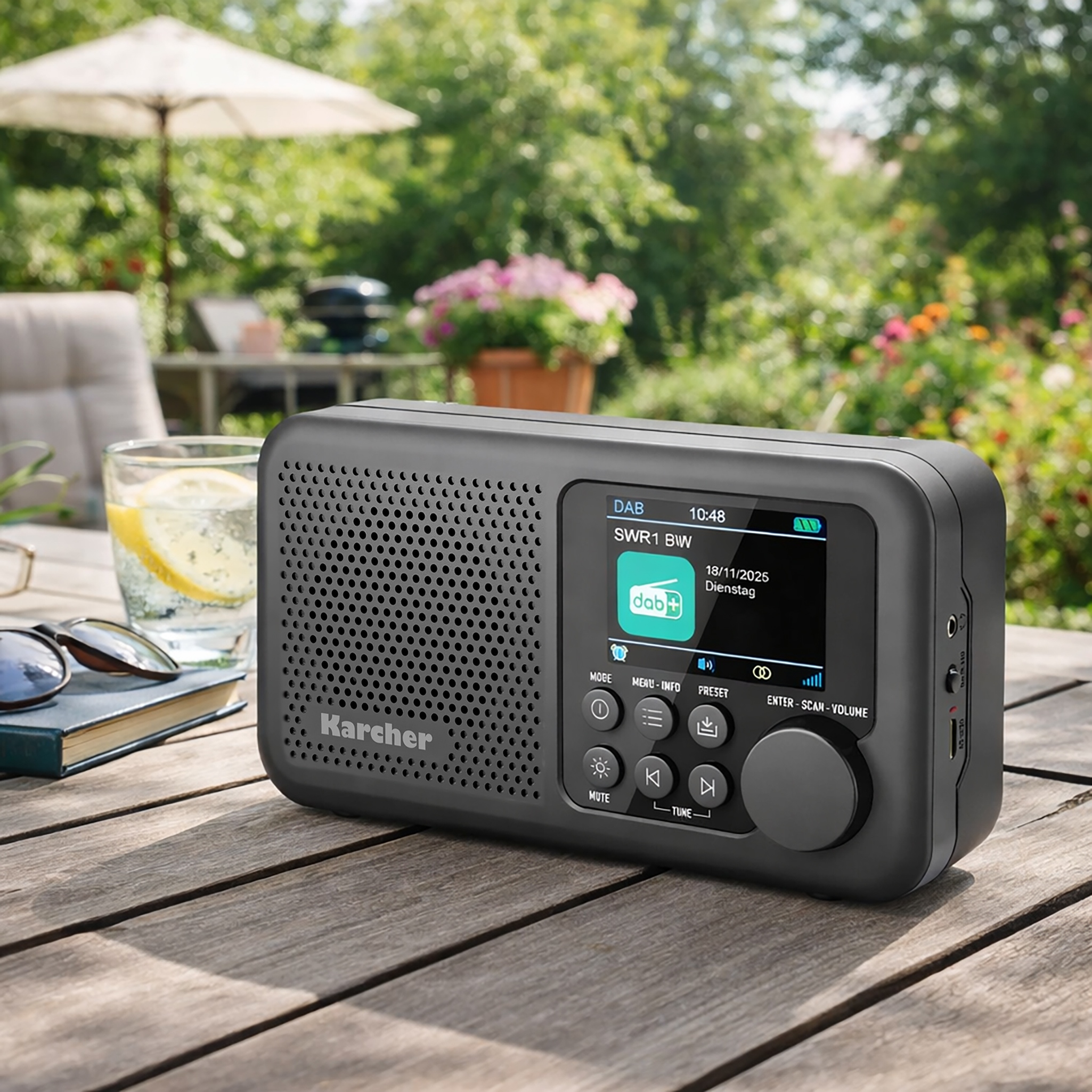 Une radio numérique Karcher noire sur une table de jardin avec un verre de limonade et des lunettes de soleil.