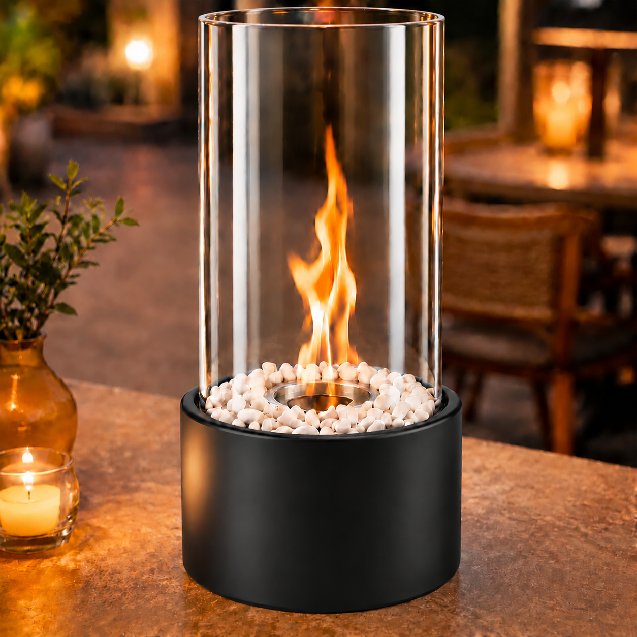 Eine Tisch-Glas-Feuerschale mit weißen Kieselsteinen und schwarzem Sockel brennt im Freien.