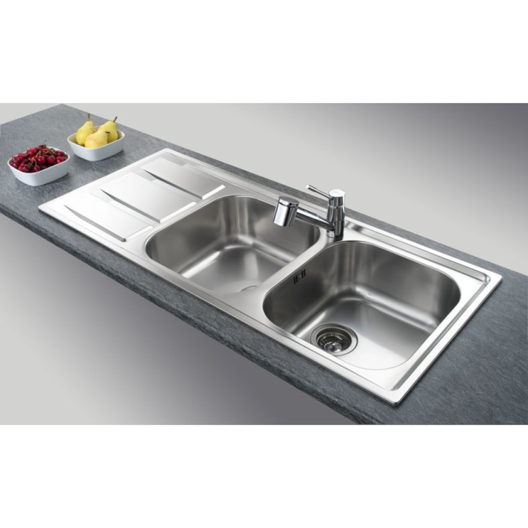 Lavello doppio in acciaio inossidabile con gocciolatoio su piano scuro e ciotole di frutta.