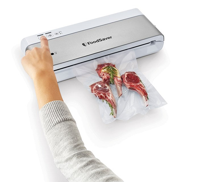 Ręka naciska przycisk na białej zgrzewarce FoodSaver, zgrzewając worek z surowymi kotletami jagnięcymi.