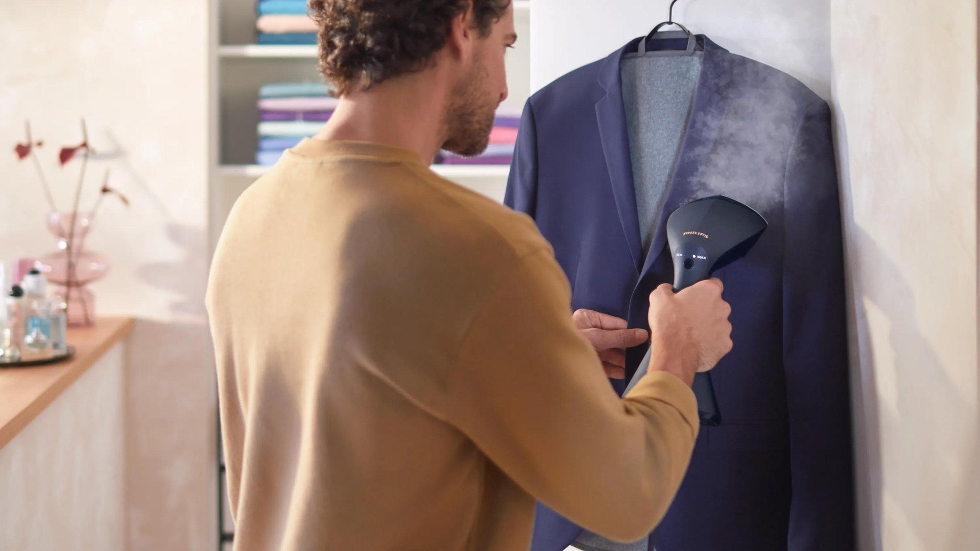 Un uomo usa un vaporizzatore per vestiti su una giacca blu appesa in una stanza.