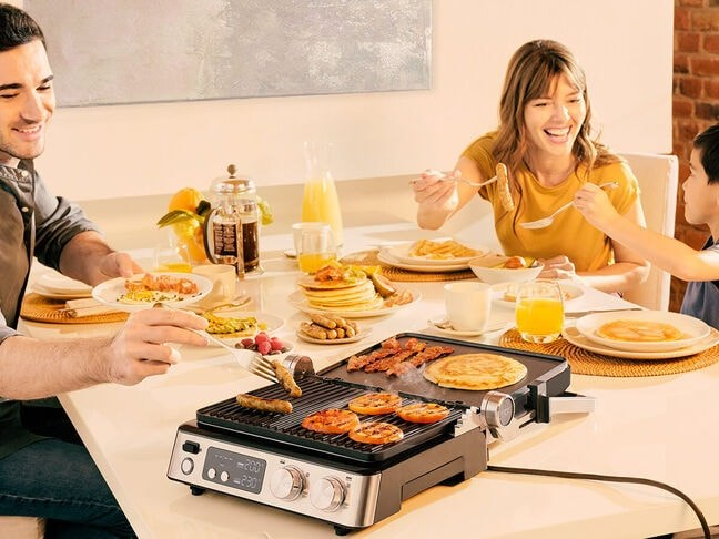 Una famiglia sorridente che fa colazione insieme, con una piastra elettrica sul tavolo.