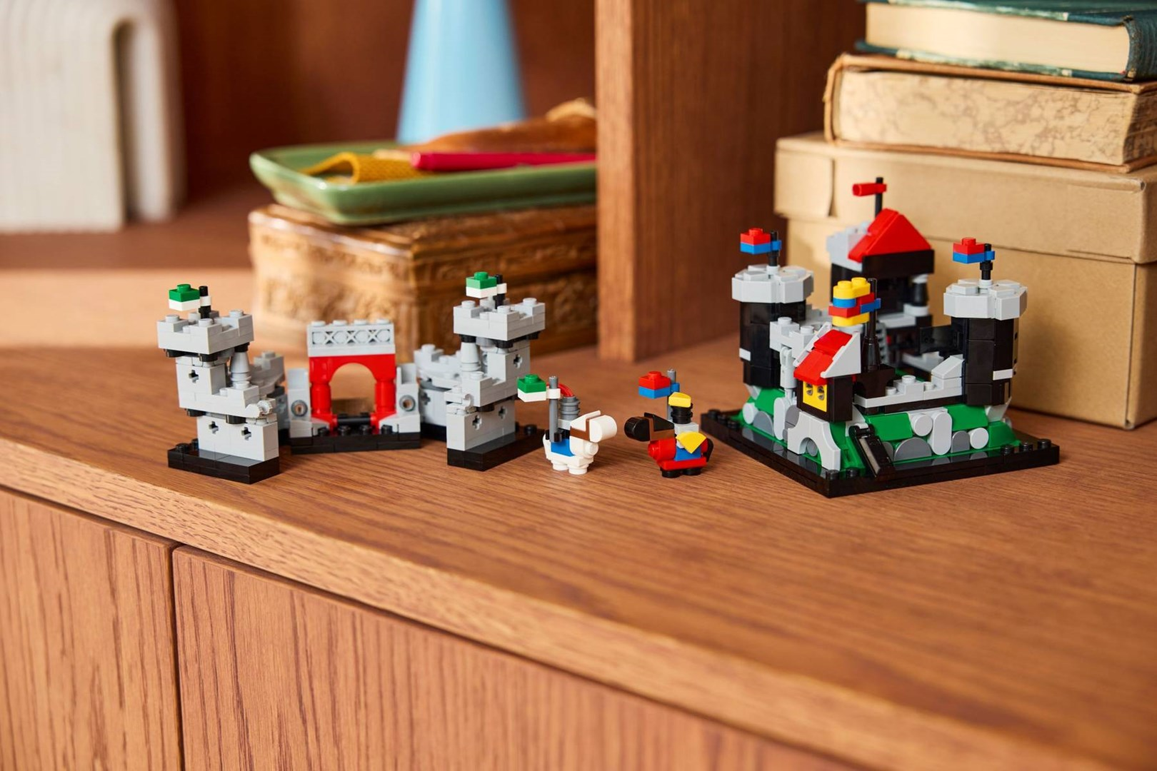 Arka planda kitapların olduğu ahşap bir rafta Lego kaleleri ve figürleri.