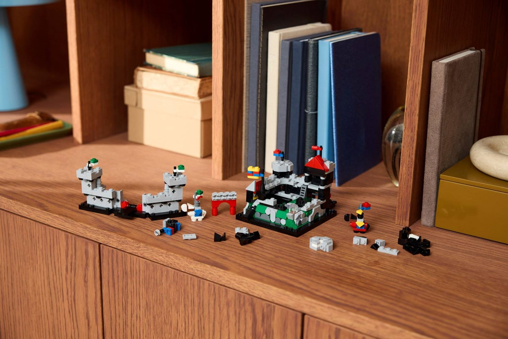 Ahşap bir masa üzerinde gri duvarları, kırmızı çatıları ve küçük figürleri olan orta çağ kalesi Lego modeli.