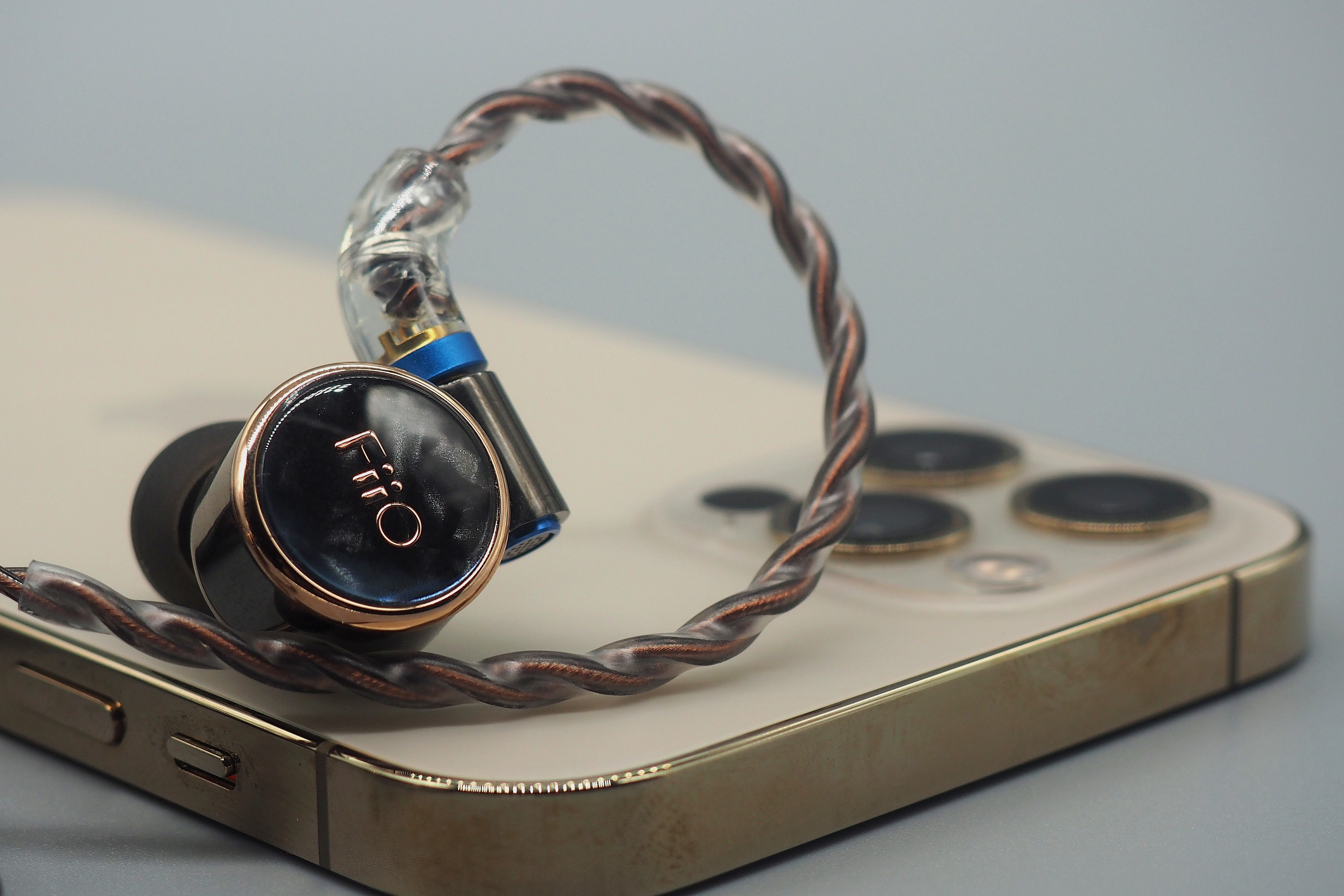 Un auricular con cable y carcasa negra y dorada descansa sobre un teléfono dorado contra un fondo gris.