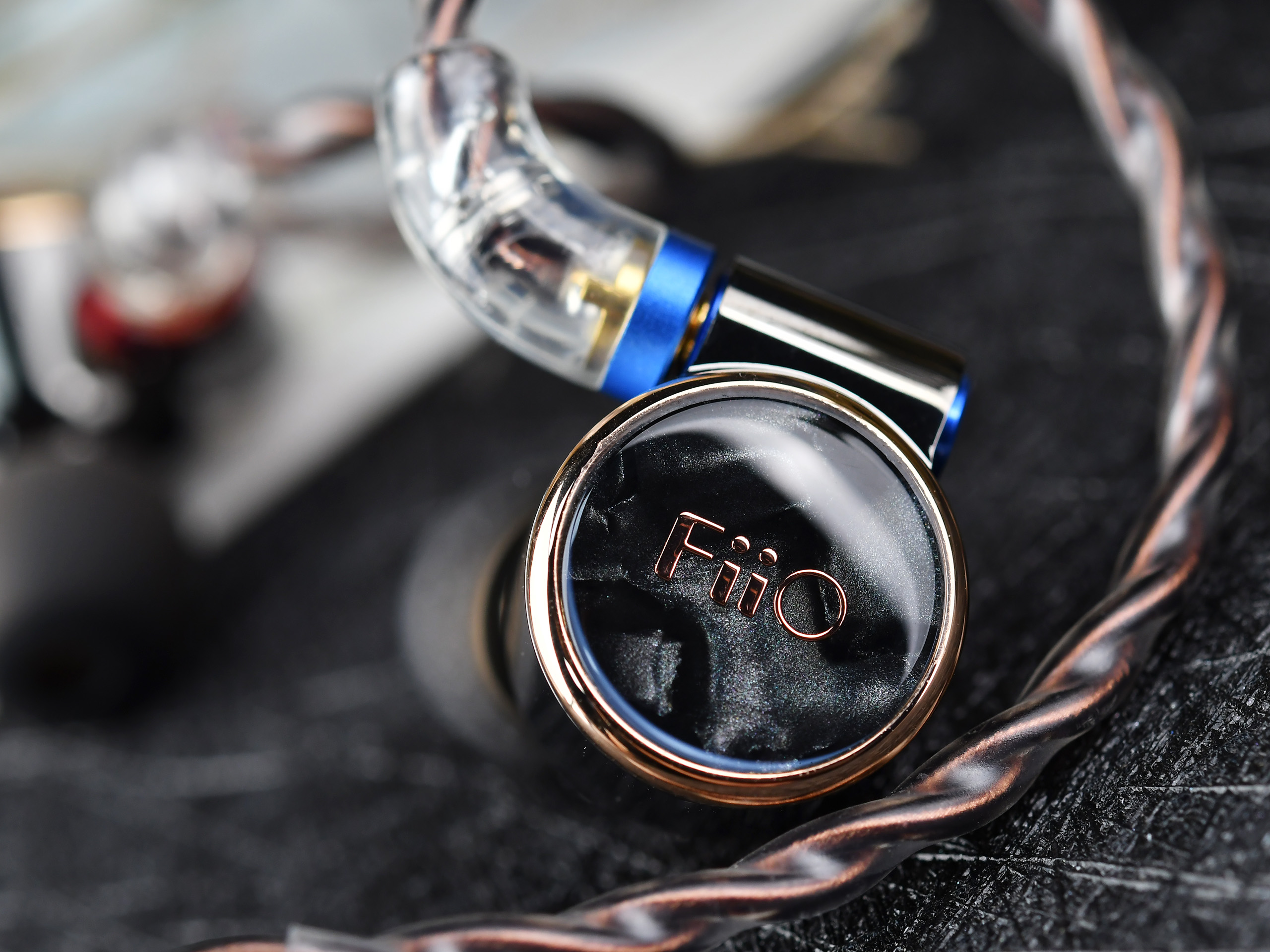 Primer plano de un monitor in-ear de alta gama con placa frontal de mármol negro, borde dorado y cable trenzado.