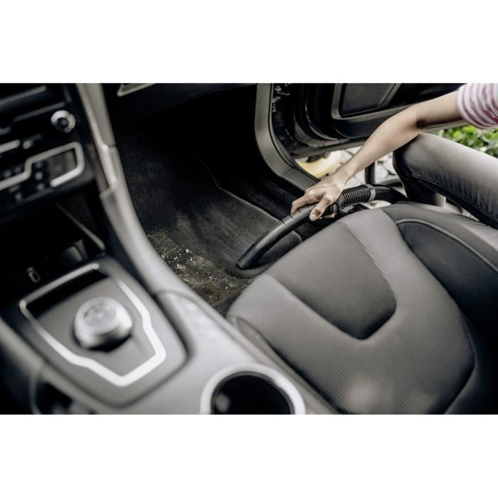 Persona aspirando la alfombra del suelo del coche usando una manguera negra.