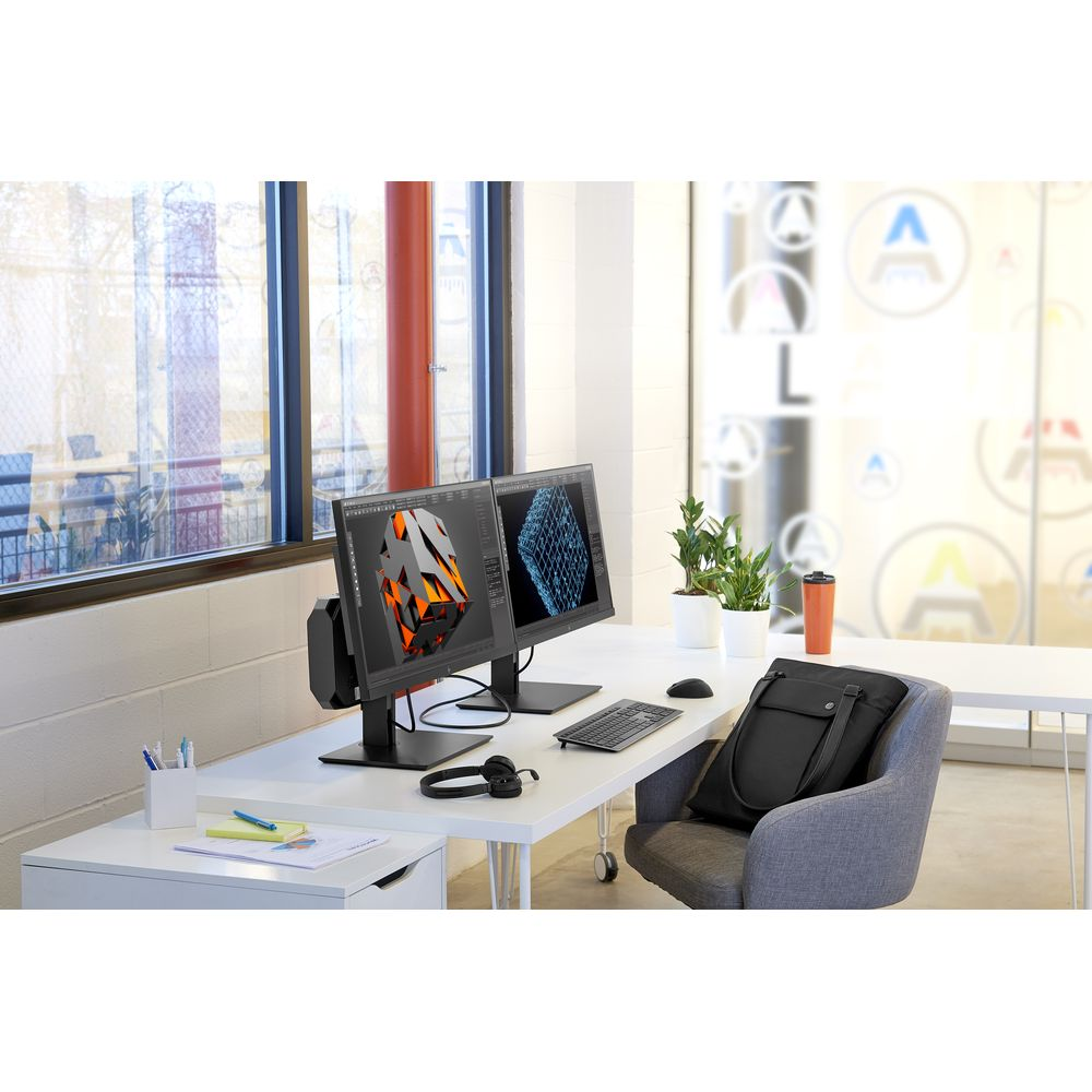 Espacio de trabajo moderno con dos monitores, teclado, ratón y una silla gris en una oficina luminosa.
