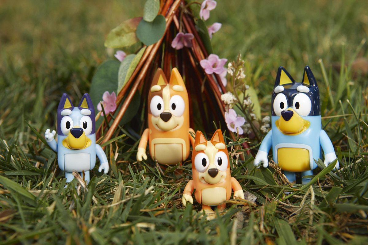 Cuatro figuras de Bluey de pie en la hierba frente a un tipi de ramitas.