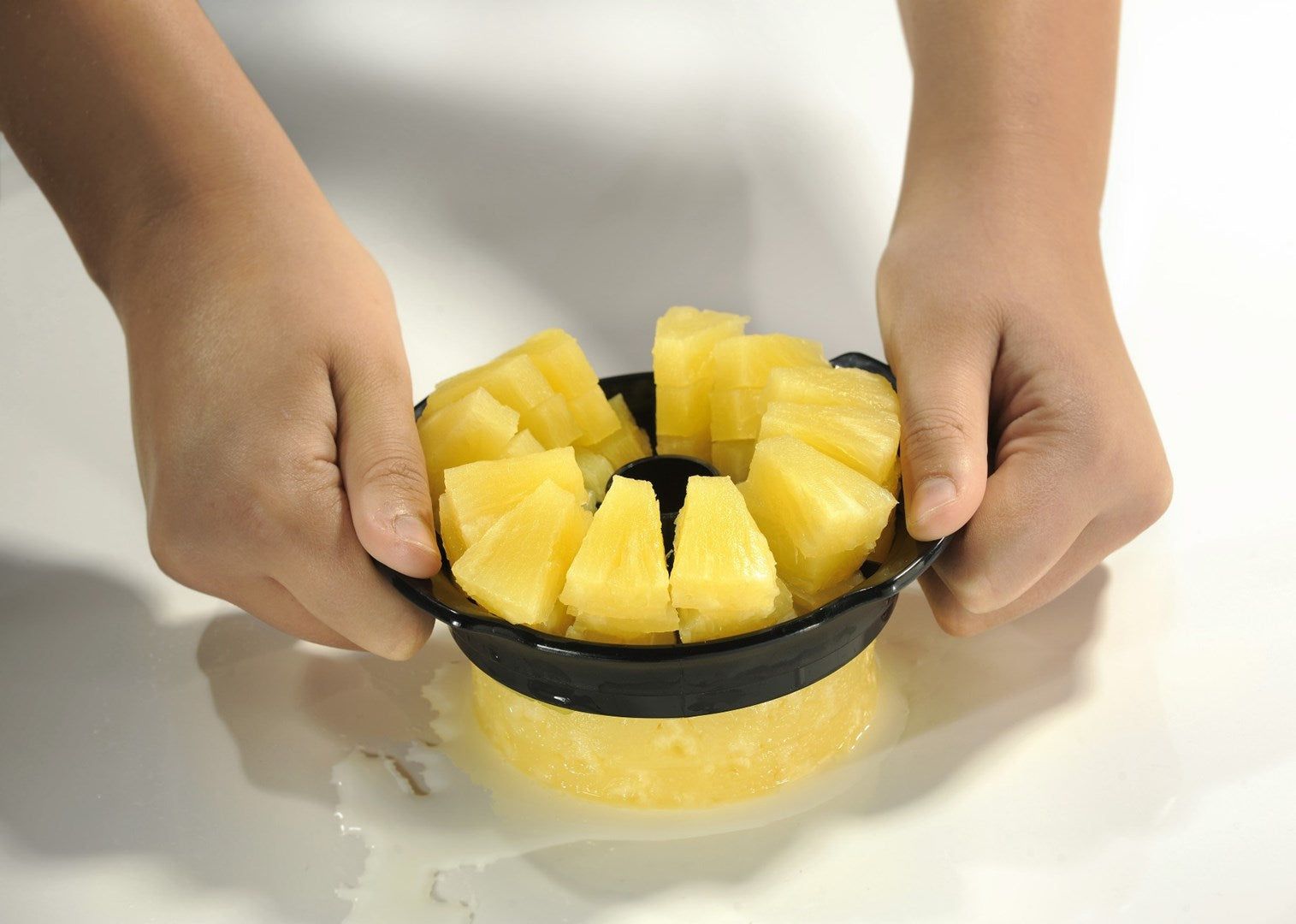 Hände halten ein schwarzes Werkzeug, das eine frische Ananas in ordentliche Stücke schneidet.
