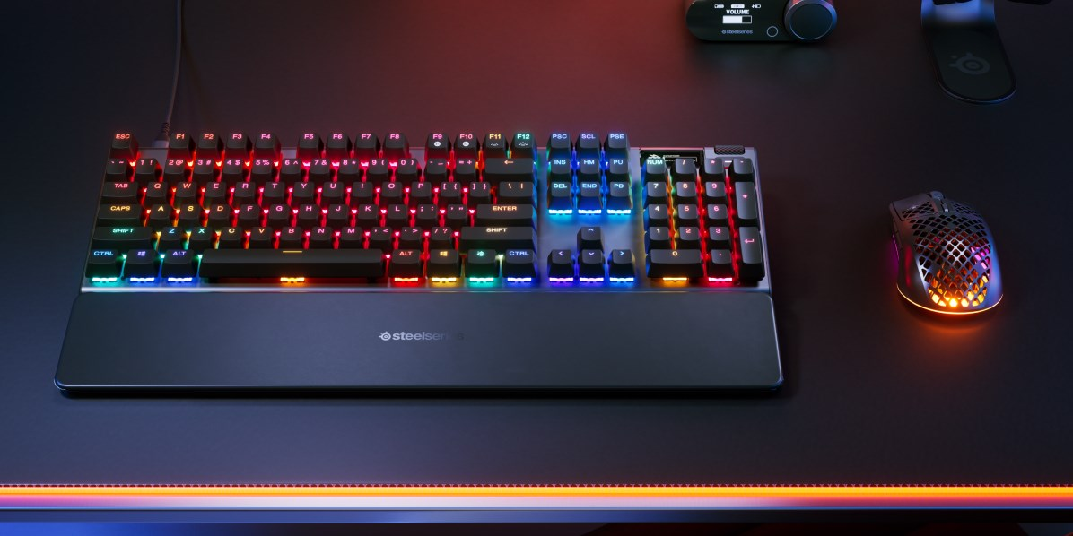 Un teclado mecánico negro con retroiluminación RGB, reposamuñecas y un ratón a juego en un escritorio oscuro.
