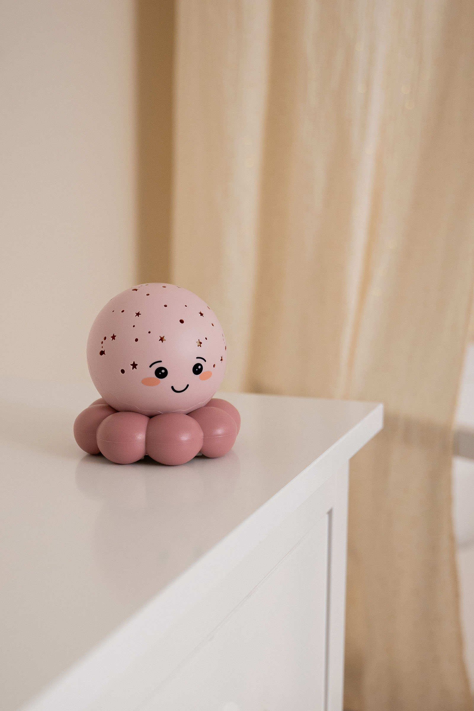 Sevimli pembe bir ahtapot gece lambası, bej perde arka planında beyaz bir rafta duruyor.