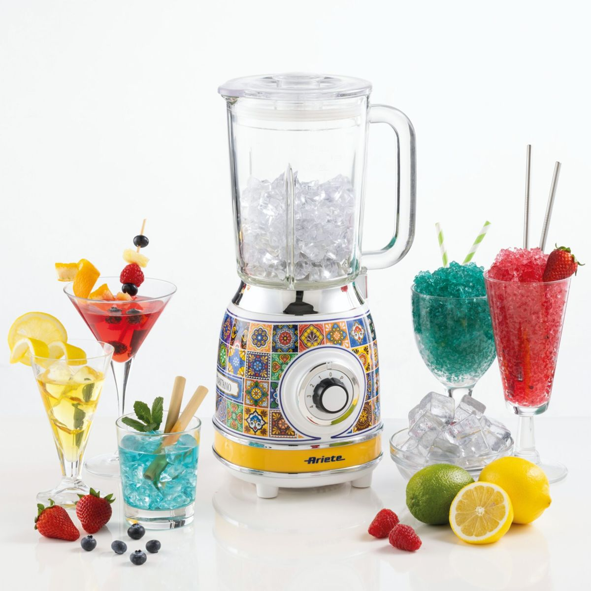 Renkli desenli beyaz bir blender, renkli kokteyller, buz küpleri ve taze meyvelerle çevrili olarak merkezde duruyor.