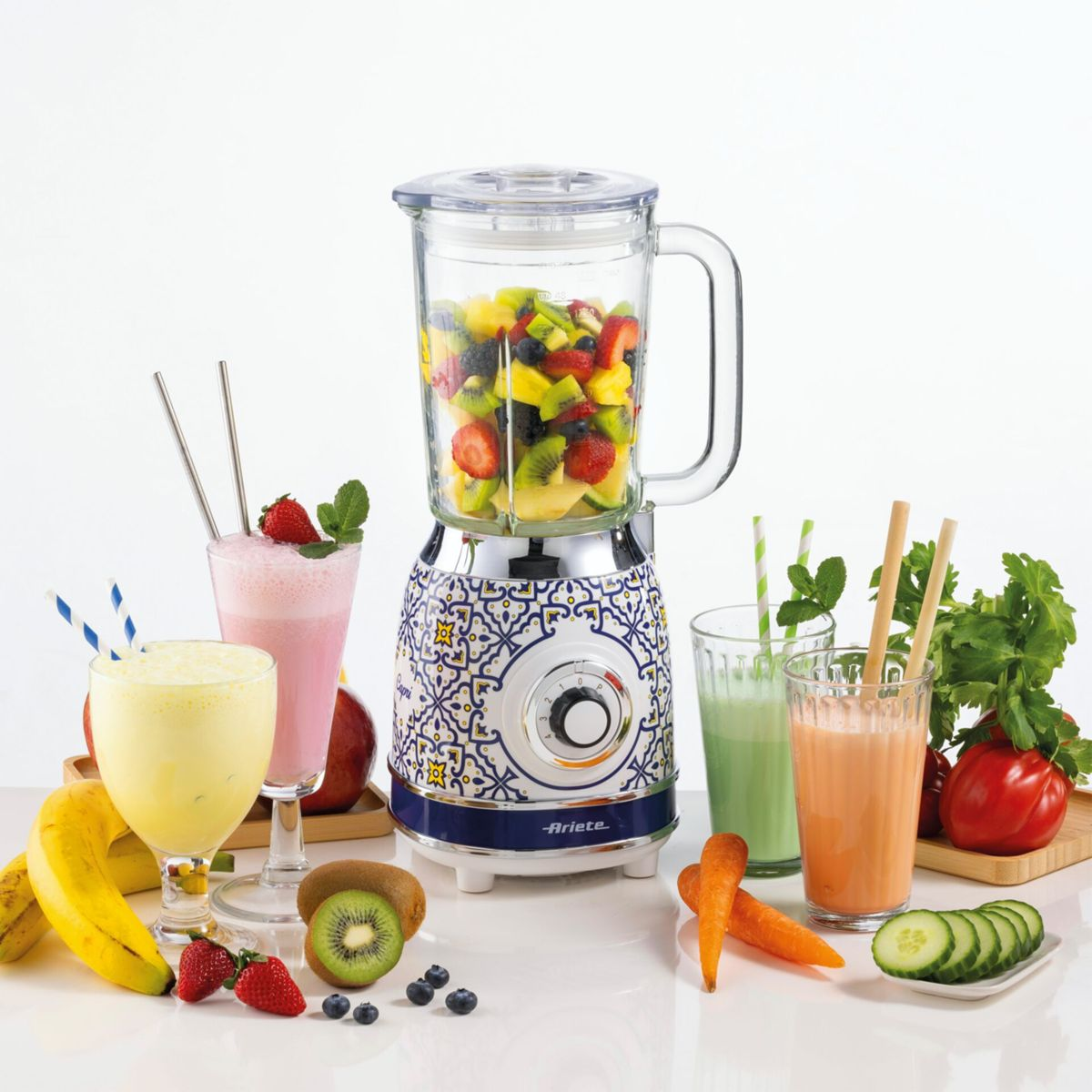 Meyveyle dolu desenli bir blender, çevresinde smoothie'ler, muzlar, meyveler ve dilimlenmiş sebzeler.