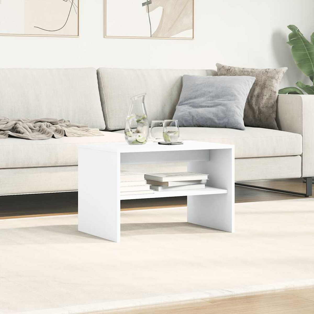 Una mesa de centro blanca con libros y una jarra se encuentra frente a un sofá beige con cojines.